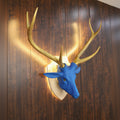Blue deer head with gold antlers mounted on a wooden wall.