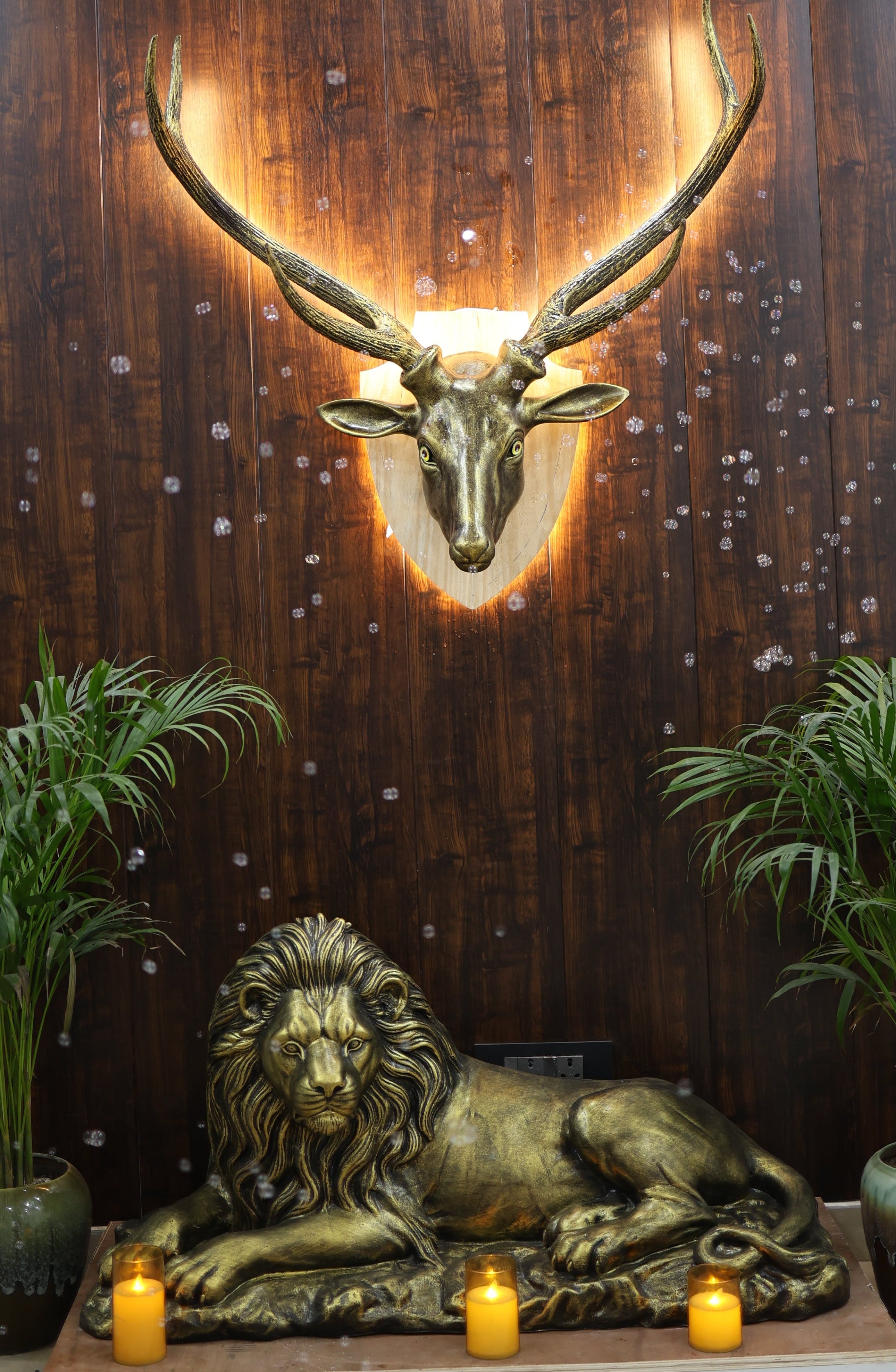 Decorative wall with a gold deer head mount, lion sculpture, and potted plants.