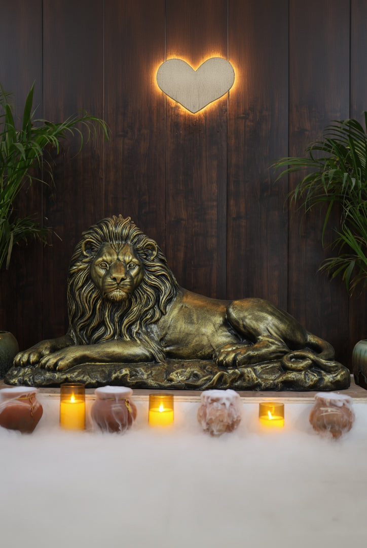 Bronze lion sculpture on a platform with lit candles and plants in the background